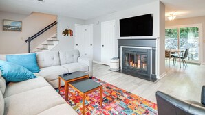 A living room with a sofa, a coffee table, a fireplace, and a TV mounted above it. - Walk to Main St Hendersonville: Chic Home w/ Yard (Hendersonville)