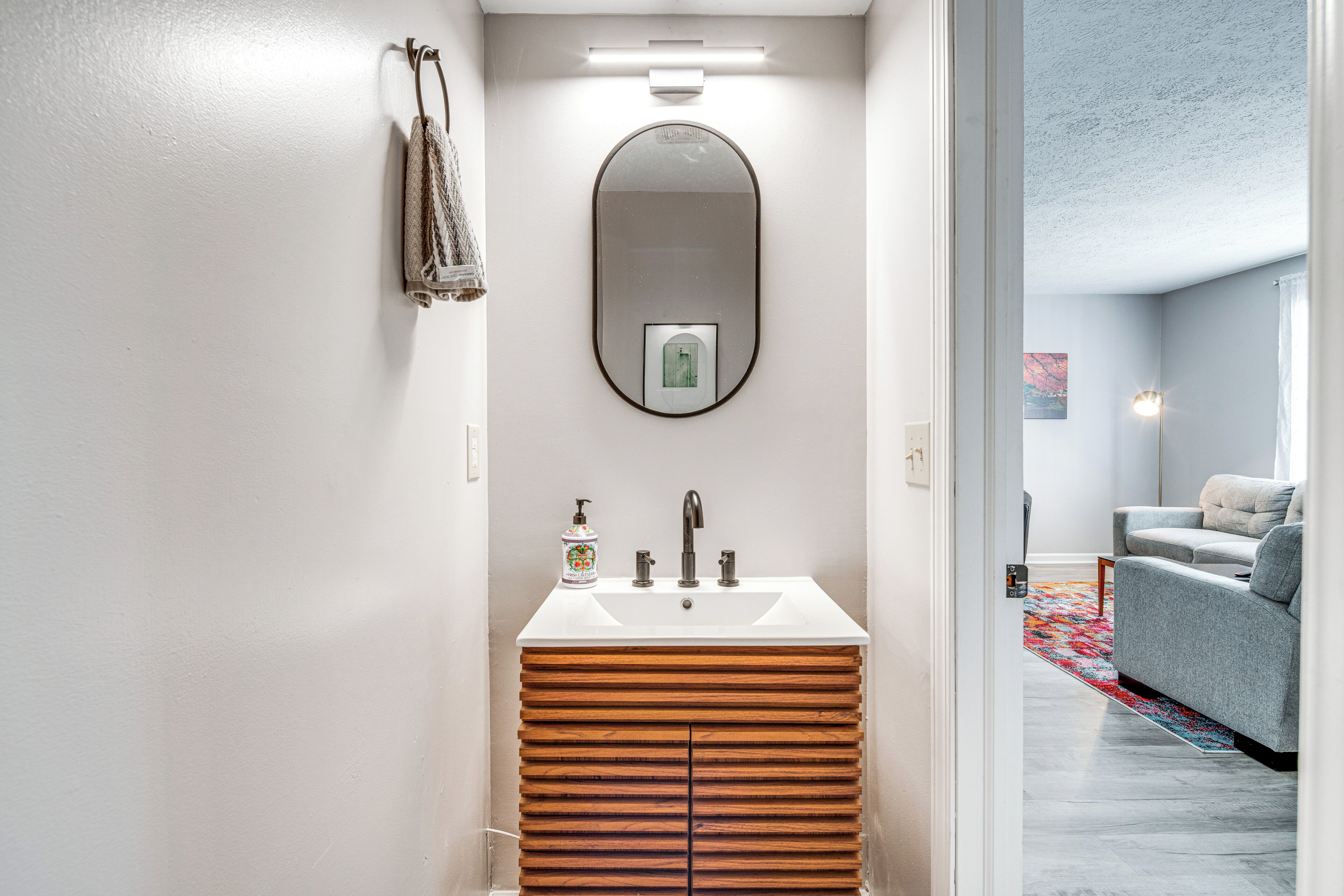 Een moderne badkamer met een houten wastafelmeubel, een grote spiegel en een witte wasbak.