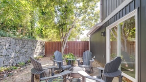 An outdoor patio with Adirondack chairs and a table, surrounded by a stone wall and a wooden fence. - Walk to Main St Hendersonville: Chic Home w/ Yard (Hendersonville)