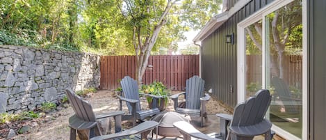 An outdoor patio with Adirondack chairs and a table, surrounded by a stone wall and a wooden fence.
