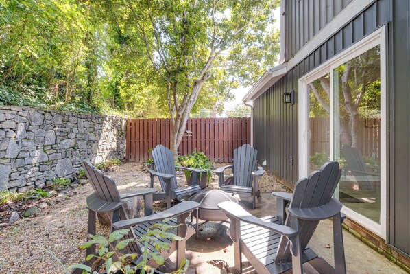 Une terrasse extérieure avec des fauteuils Adirondack et une table, entourée d’un mur de pierres et d’une clôture en bois.
