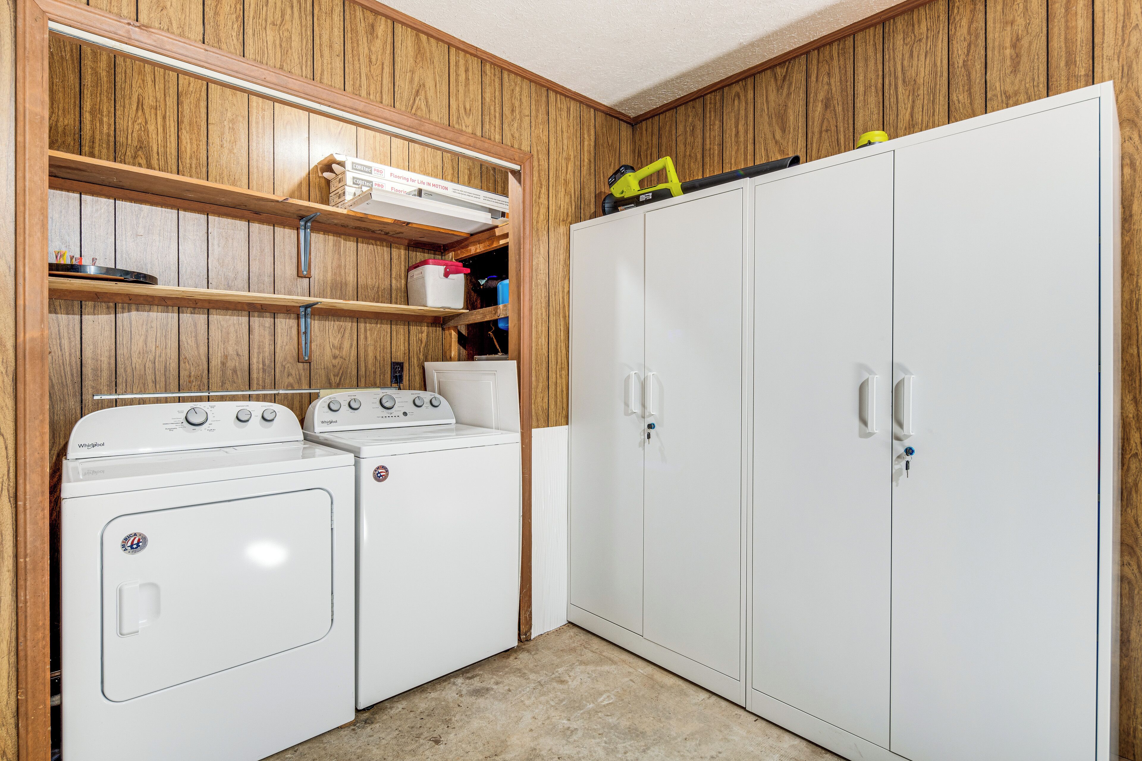 Une buanderie équipée de deux machines à laver à chargement frontal, d’étagères en bois et d’une armoire blanche.