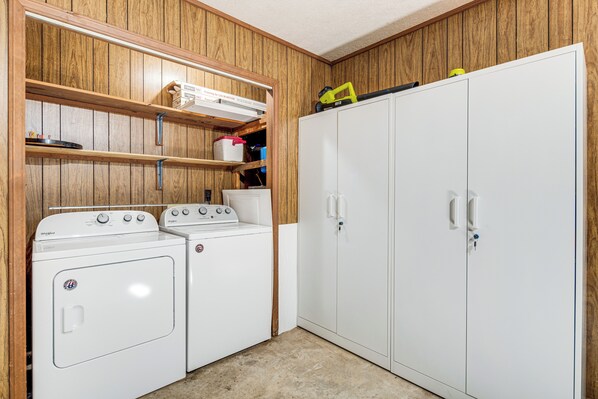 Une buanderie équipée de deux machines à laver à chargement frontal, d’étagères en bois et d’une armoire blanche.