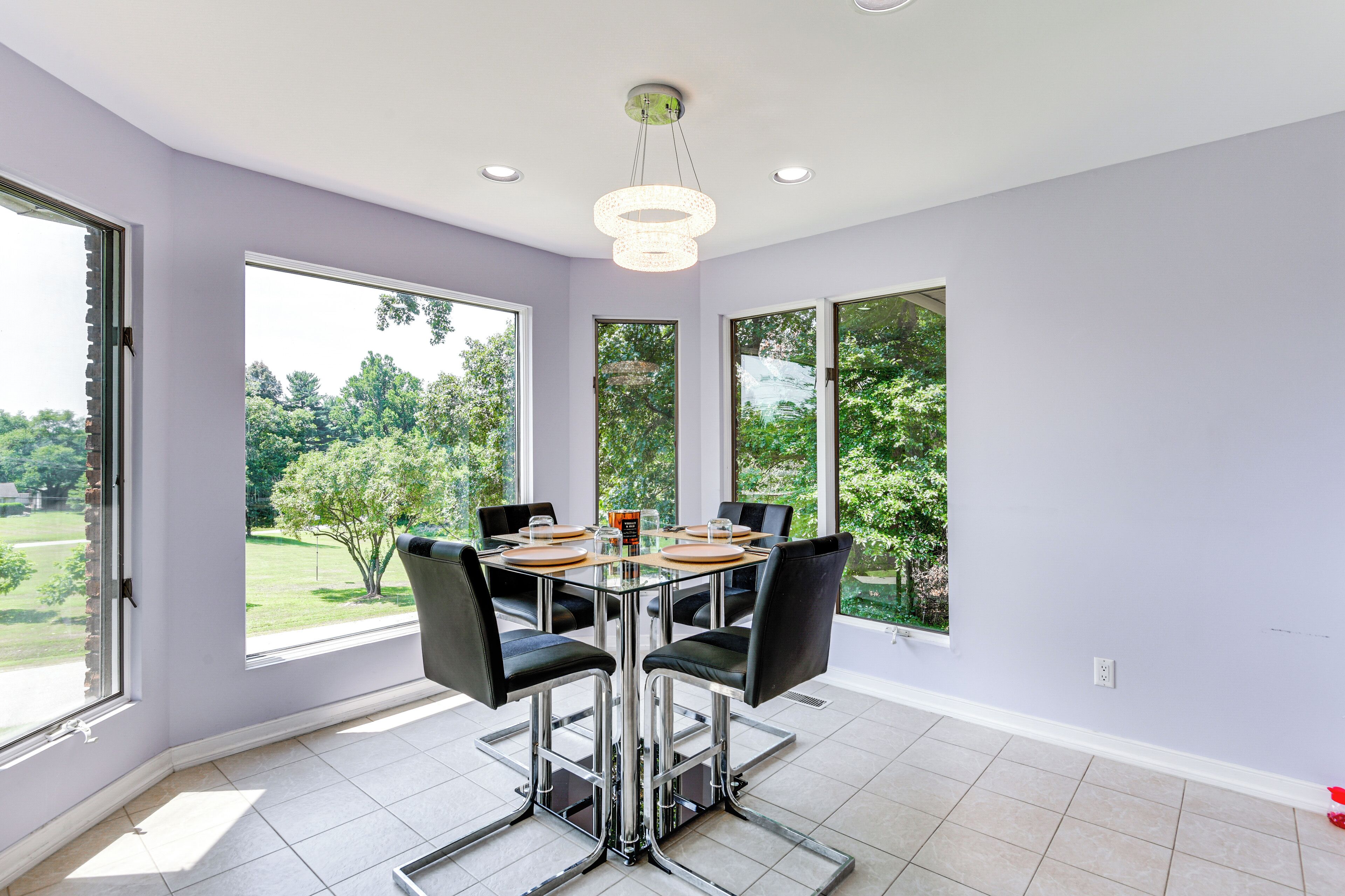 A dining area with a glass table and chairs, large windows, and a ceiling light fixture.