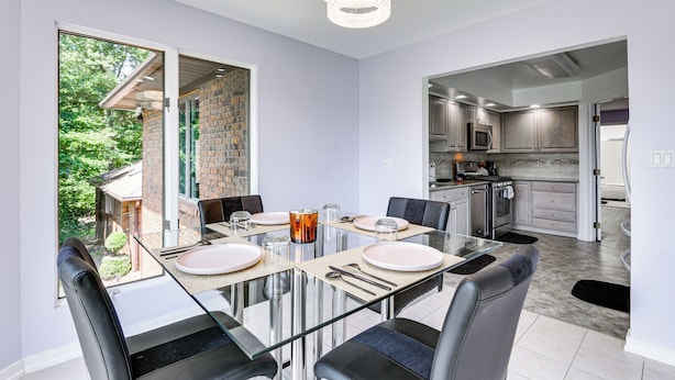Un comedor moderno con una mesa de vidrio, sillas negras y vistas al jardín.