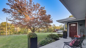 A front porch with a black planter, a chair with patterned cushions, and a red door. - 1/2 Mi to Creation Museum: Home w/ Large Yard! (Petersburg)
