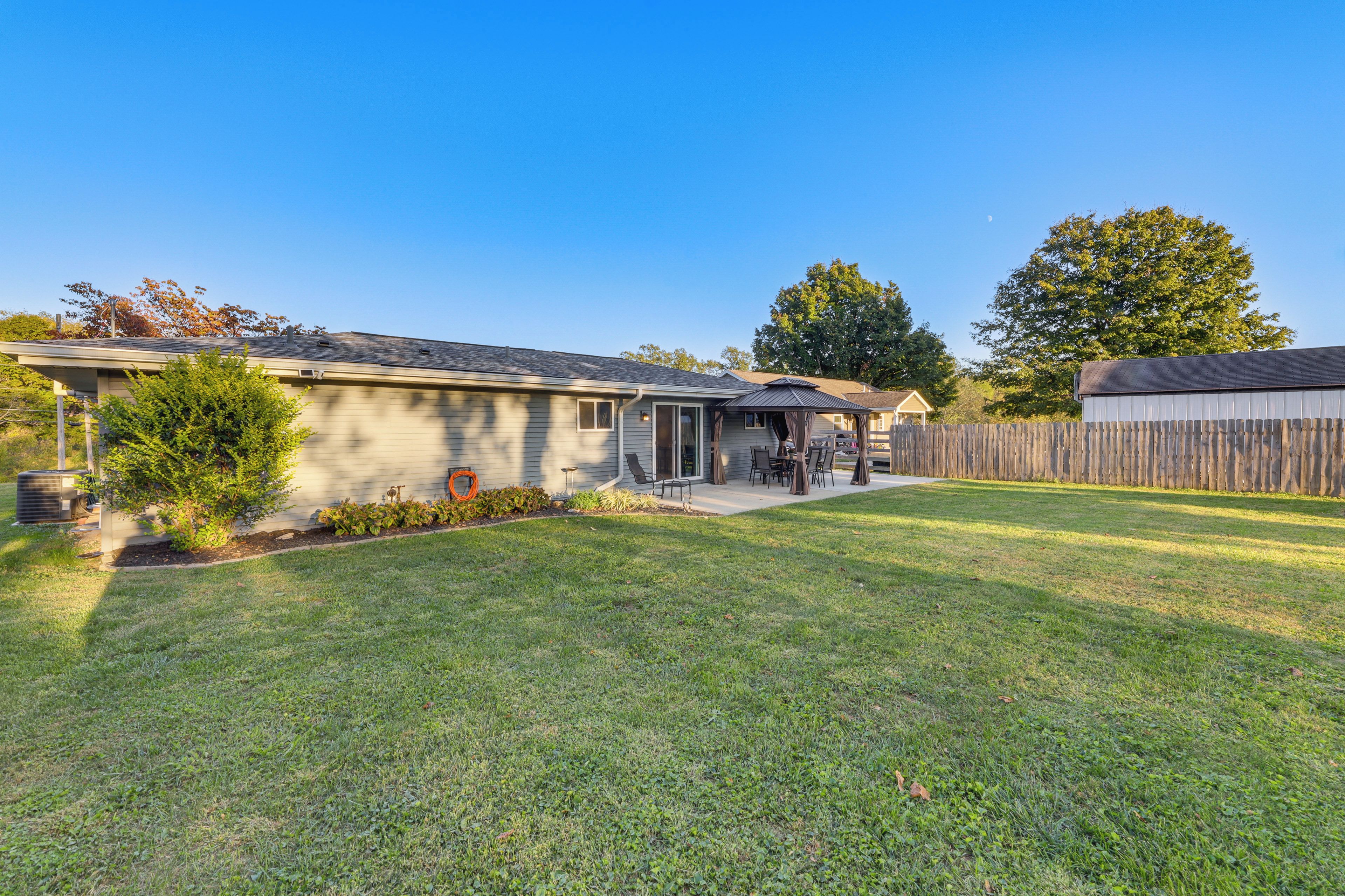 A residential house with a front yard, a patio with outdoor furniture, and a wooden fence.