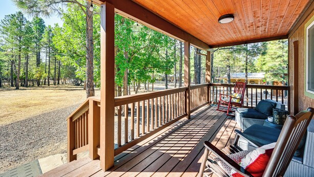A covered porch with wooden railings, outdoor furniture, and a view of a forested area. - Hike, Boat & Fish: Serene Cabin in Happy Jack (Happy Jack)