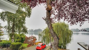 Un coche rojo aparcado en una entrada con vistas a un lago y árboles.