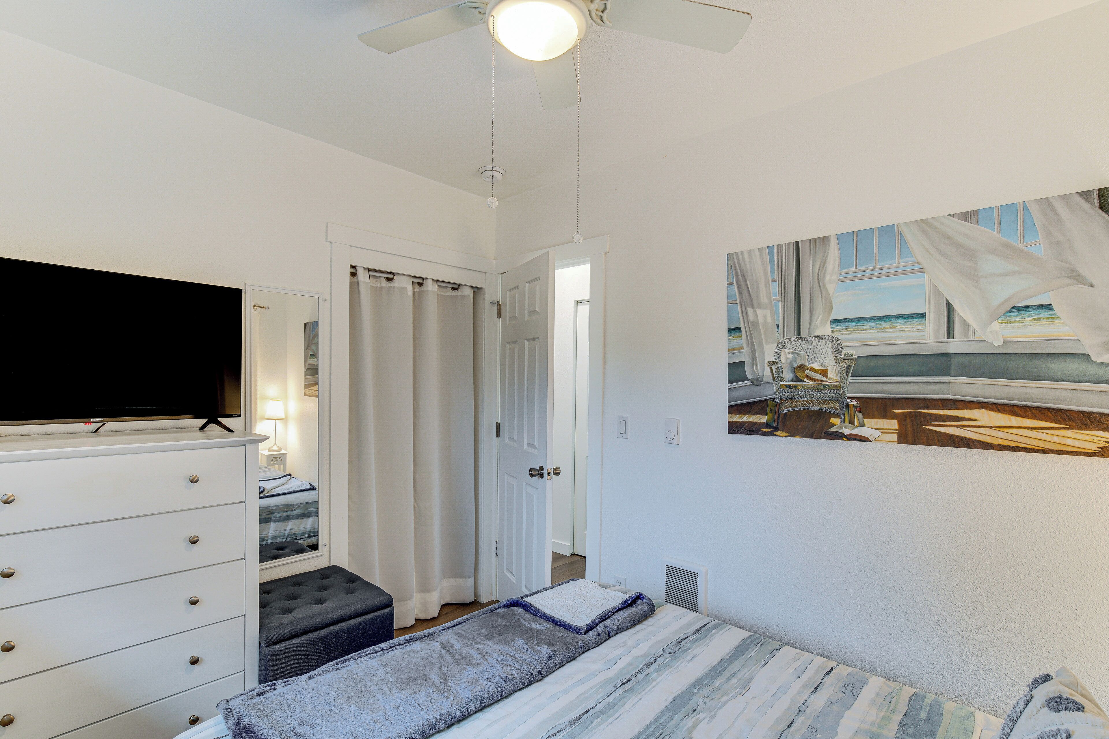 A bedroom with a bed, a dresser, a television, and a painting of a beach scene.