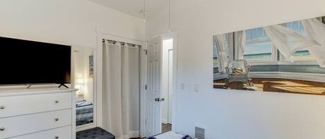 A bedroom with a bed, a dresser, a television, and a painting of a beach scene.