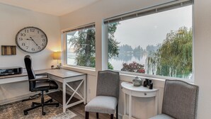 Una habitación con escritorio, una silla, un reloj y vista a un lago.