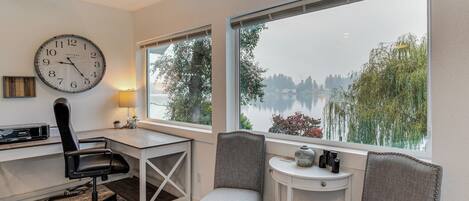 Ein Zimmer mit Schreibtisch, Stuhl, einer Uhr und Seeblick.
