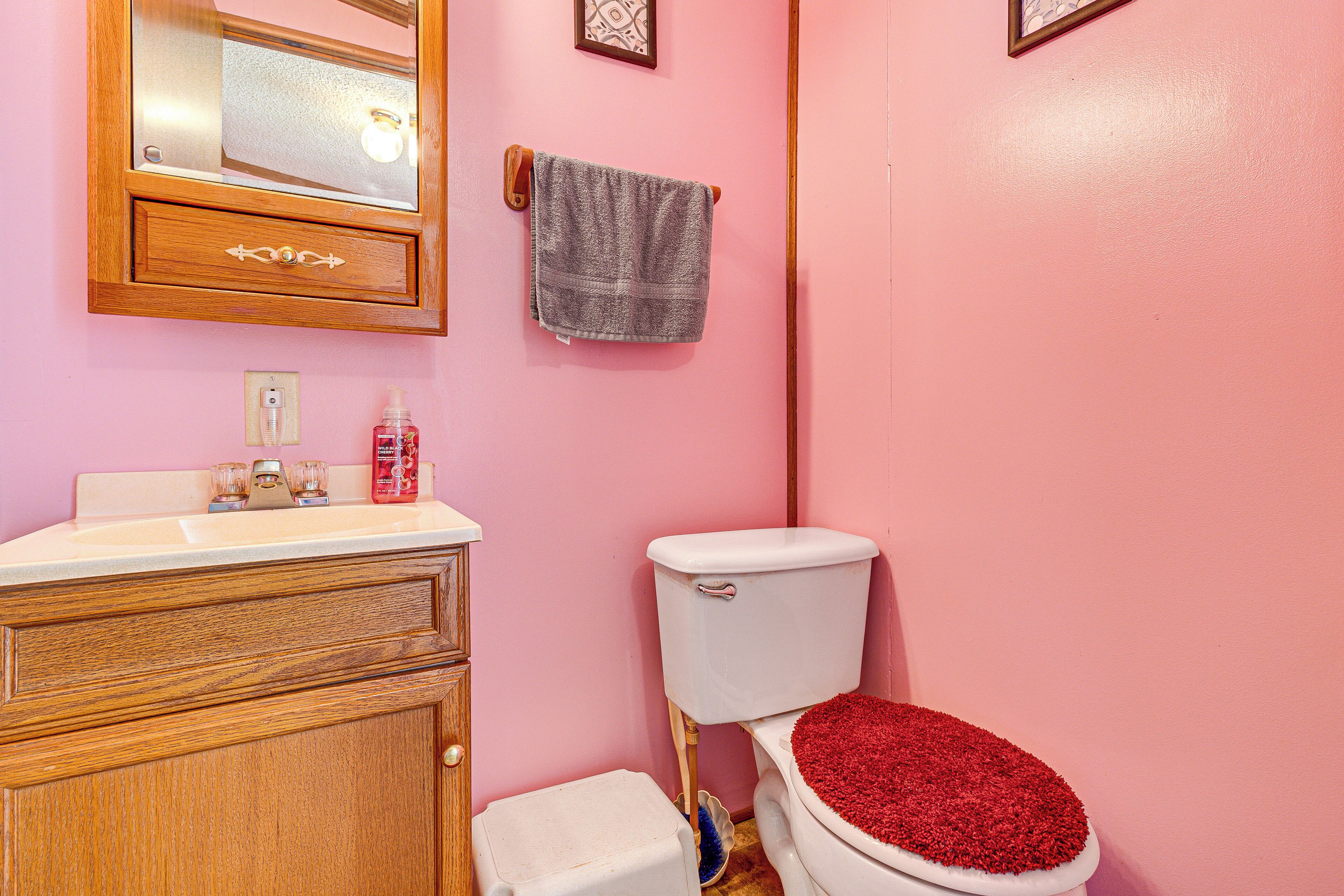Un baño con paredes rosas, un tocador de madera, un inodoro blanco con tapa roja y una toalla colgada en la pared.