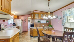 A kitchen with wooden cabinets, a central island, and a dining area with a round table and chairs. - Paden City Home Near Ohio River! (Paden City)