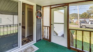 A covered porch with a green artificial turf, a wooden door, and a view of a parked vehicle through a glass door. - Paden City Home Near Ohio River! (Paden City)