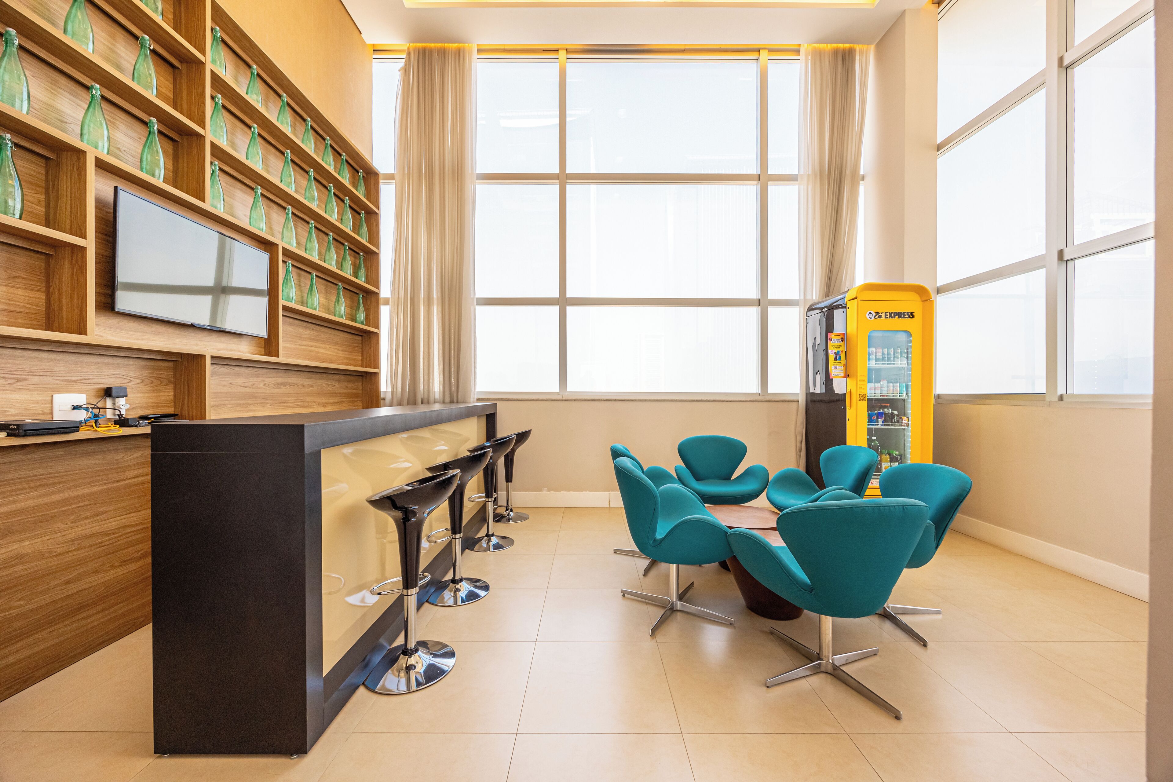 A modern lobby with a reception desk, a TV, a vending machine, and teal chairs.