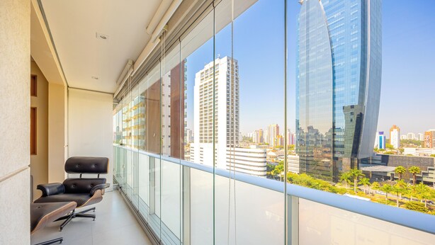 Un balcon avec un fauteuil moderne, de grandes fenêtres et une vue sur la ville.