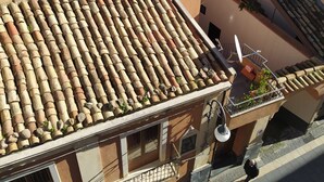 A residential building with terracotta tiled roofs, balconies with railings, and a person walking on the street below. - "The Tailoring" a thread of history in the heart of the country (Centuripe)