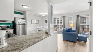 A modern kitchen with built-in appliances, a dining area with a blue sofa, and a view of the outdoors through large windows. - B325 at the Myrtle Beach Resort (Myrtle Beach)