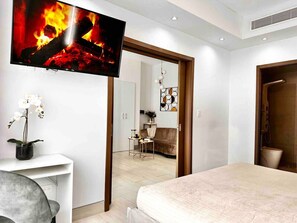 Una habitación de hotel moderna con una cama grande, un televisor de pantalla plana montado en la pared, un escritorio pequeño con una silla y una orquídea en maceta.