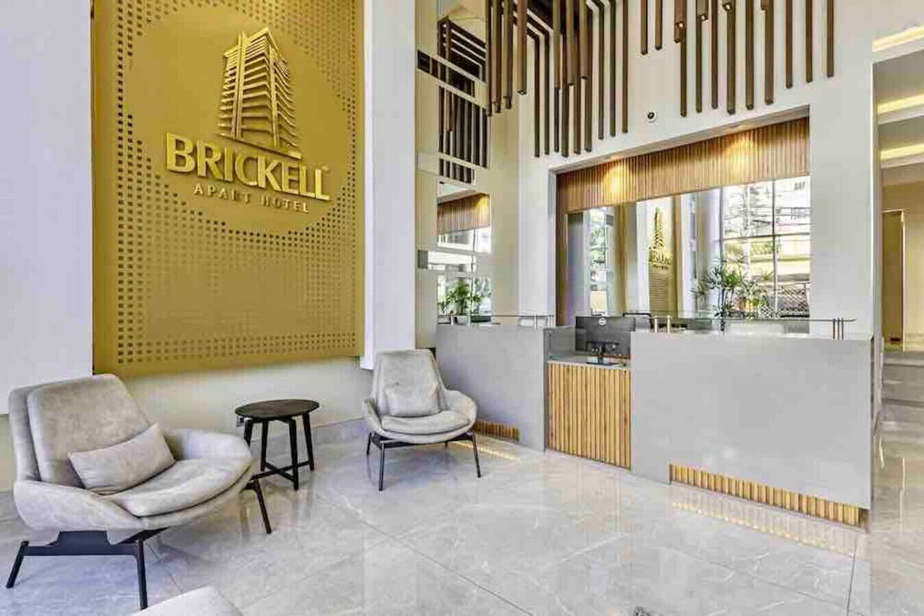 Een receptiegedeelte met een modern ontwerp, met een receptiebalie, twee fauteuils en een logo van Brickell Apartment Hotel dat aan de muur is bevestigd.
