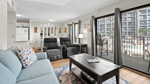 A modern living room with a sofa, armchairs, a coffee table, and a view of a parking area through large windows.