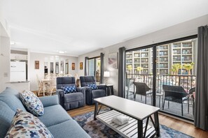 Una sala de estar moderna con un sofá, dos sillones, una mesita de centro y un balcón con mobiliario exterior.