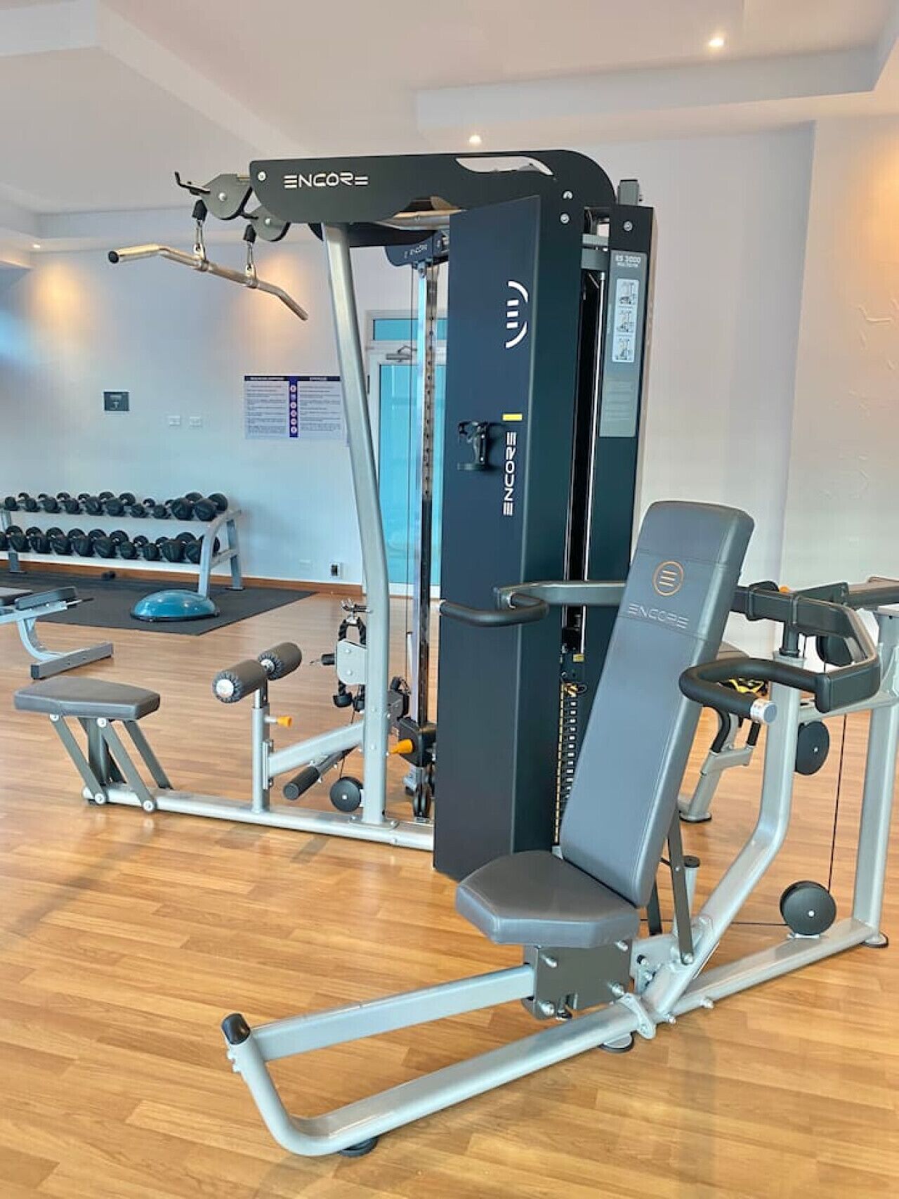Ein Fitnessstudio mit verschiedenen Trainingsgeräten, darunter eine Hantelbank, Kurzhanteln und ein Krafttrainer.