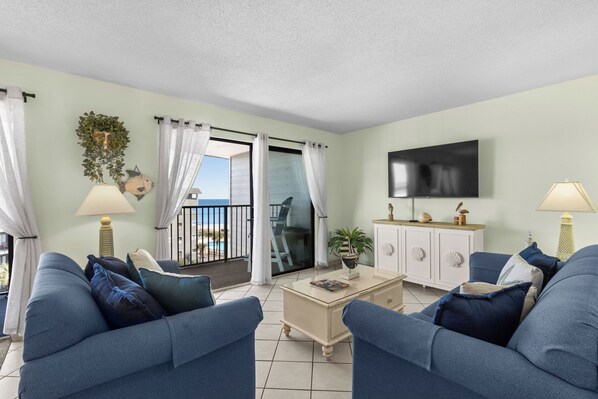 Una sala de estar con sofá, mesa de centro, televisor y vistas al exterior.