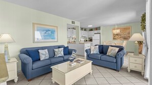 A living room with two blue sofas, a coffee table, and a kitchen in the background. - B515 Charming 2BR Condo | Ocean Views + Steps to Indoor Pool (Myrtle Beach)