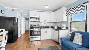 A compact kitchen with white cabinets, a black refrigerator, and a blue sofa with patterned cushions.