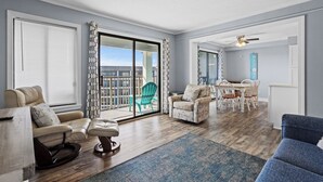Een ruime woonkamer met een grote schuifpui naar een balkon, een eethoek met tafel en stoelen, en een blauwe bank.
