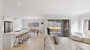 A modern kitchen with a central island, bar stools, and a dining area with a view of the backyard. - SaltCove with spa in Cowes (Cowes)