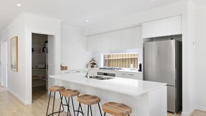 A modern kitchen with white cabinetry, a stainless steel refrigerator, and a central island with stools. - SaltCove with spa in Cowes (Cowes)
