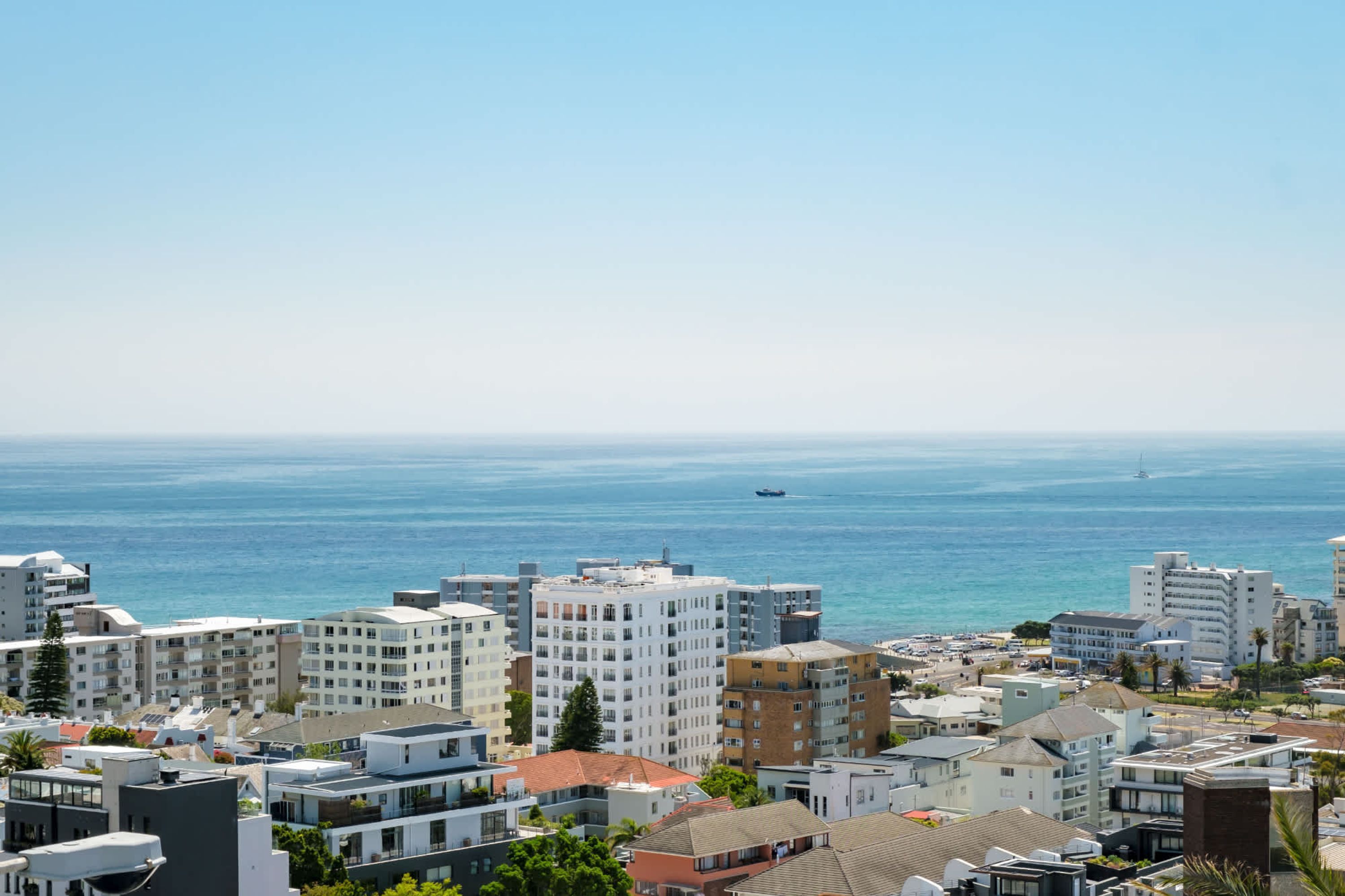 A coastal cityscape with modern buildings, a clear view of the sea, and a distant boat.