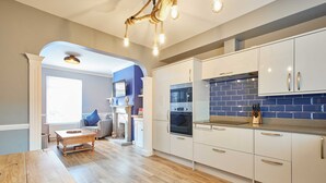A modern kitchen with white cabinets, a blue tiled backsplash, and a wooden dining table.
