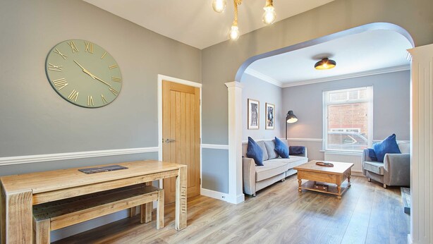 A spacious living room with a wooden bench, a round wall clock, a sofa, and a coffee table.