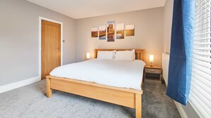 A bedroom with a wooden bed, a nightstand, a wall-mounted lamp, and a door.