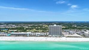 Un paysage urbain côtier avec un hôtel imposant, caractérisé par une grande tour centrale, un accès direct à la plage et une végétation luxuriante environnante.