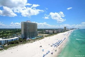 A beachside hotel with a large building, a sandy beach, and clear blue waters.