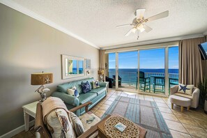 A spacious living room with a large window offering a view of the ocean, a ceiling fan, and a sofa with decorative pillows. - FREE Golf&Perks! Beachfront Boardwalk 1005 King Master, Hot Tubs, Heated Pool (Panama City Beach)