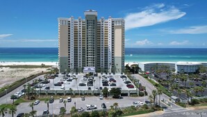 Un grand hôtel avec de nombreux étages, doté d’un parking à l’avant, offrant une vue sur une plage et l’océan.