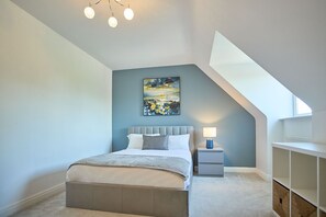 Une chambre à coucher avec un lit, une table de chevet, une lampe, un tableau et un plafond en pente.