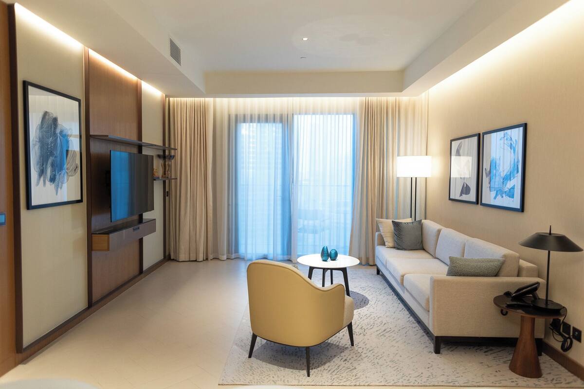 A hotel room with a sofa, armchair, TV, and artwork.