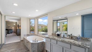 A modern bathroom with a large bathtub, a granite countertop, and a stone wall.