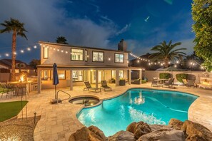 A modern house with a swimming pool, outdoor seating, and string lights.