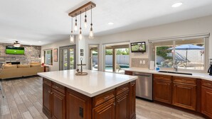 A modern kitchen with a large island, wooden cabinets, and a stone backsplash.