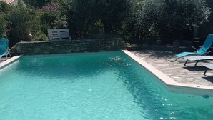 Una piscina limpida con pareti in pietra e un bordo in pietra. Sono presenti sedie a sdraio e una parete in pietra con un vaso.