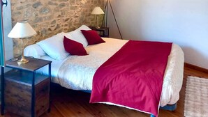 Una camera da letto con parete in pietra, un letto con biancheria da letto bianca e rossa, una coperta rossa, una lampada da comodino e una lampada da terra.
